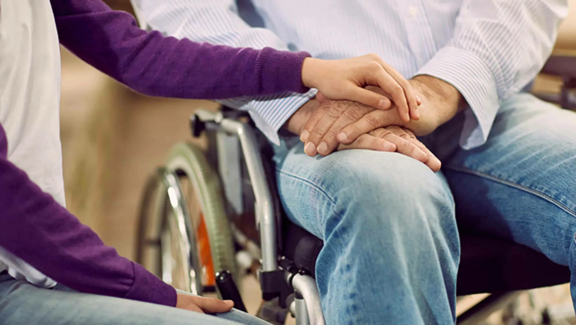 Hands embraced in the lap of a person in a wheelchair.