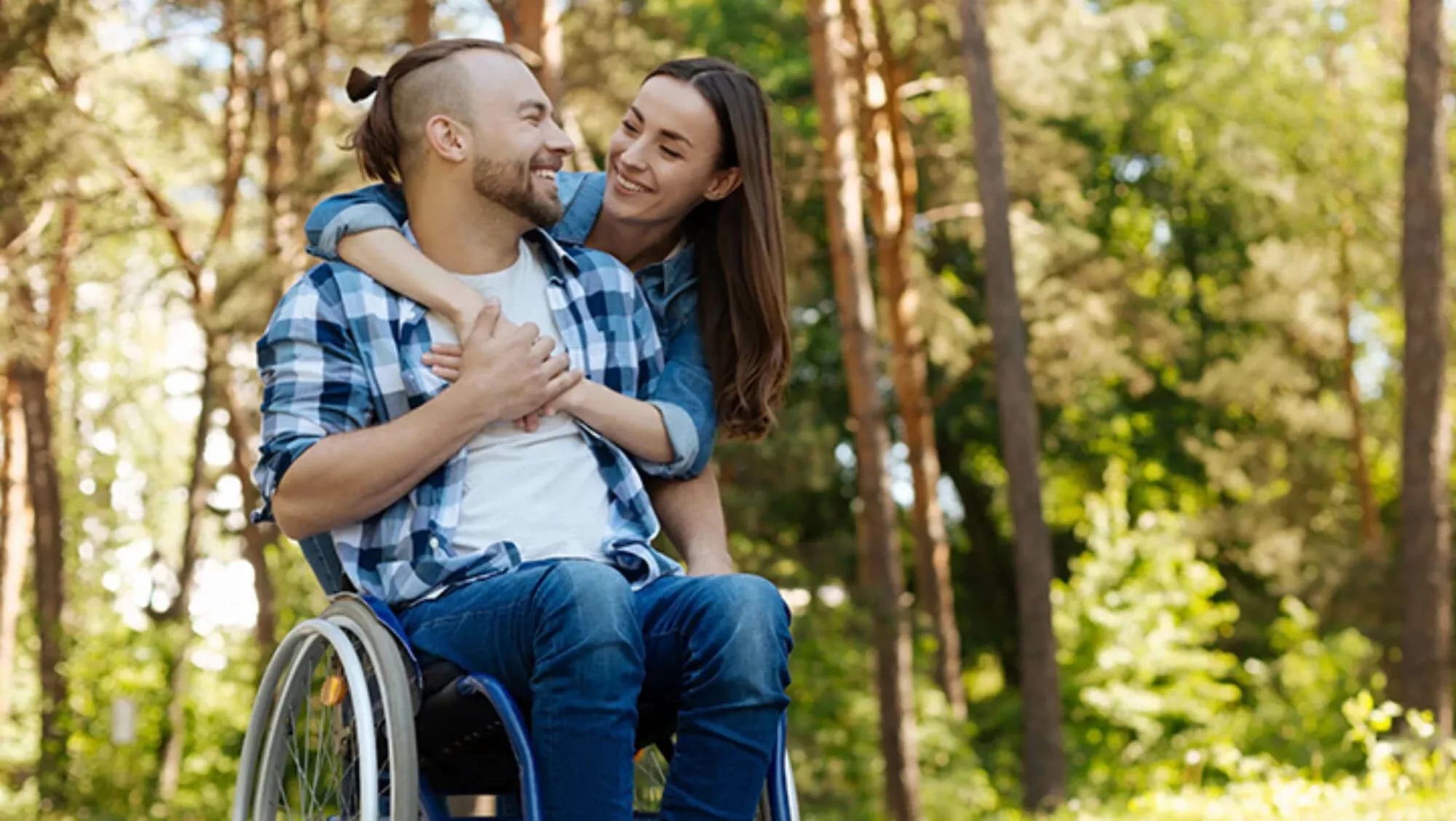 Woman hugging a man in a wheelchair from behind.