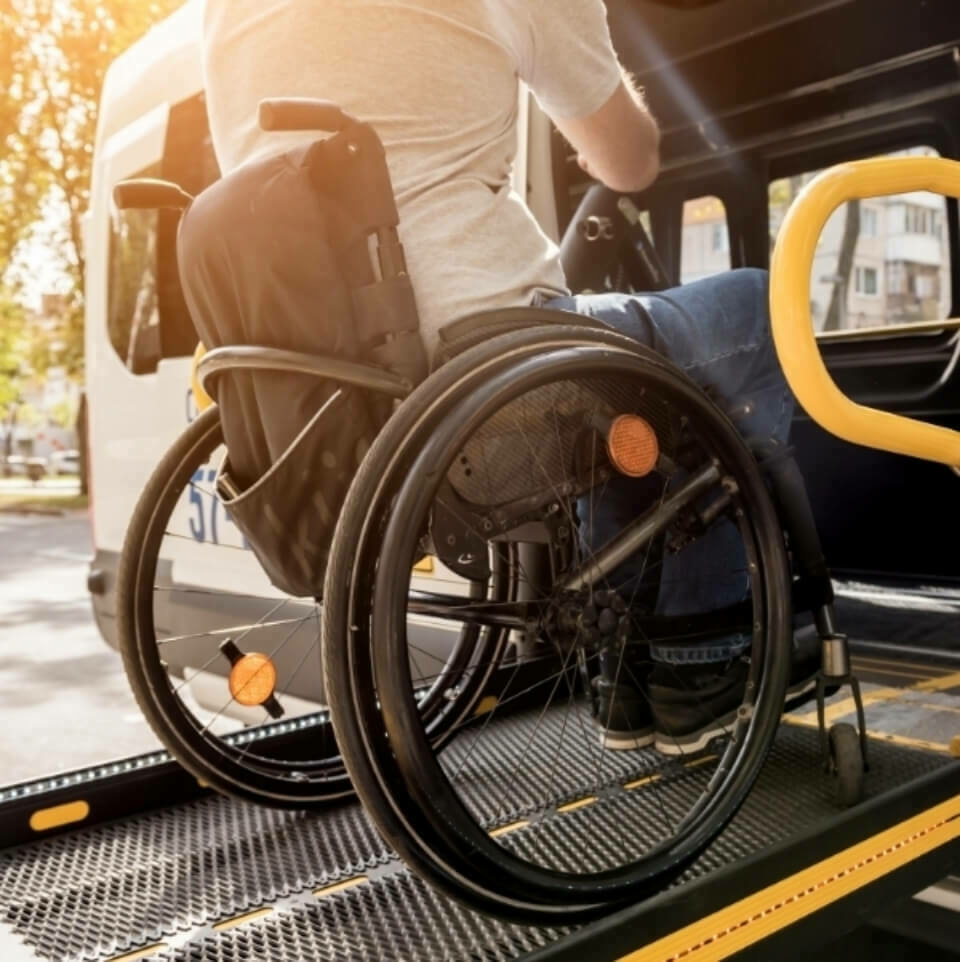 Person in wheelchair being machine-lifted into a vehicle.