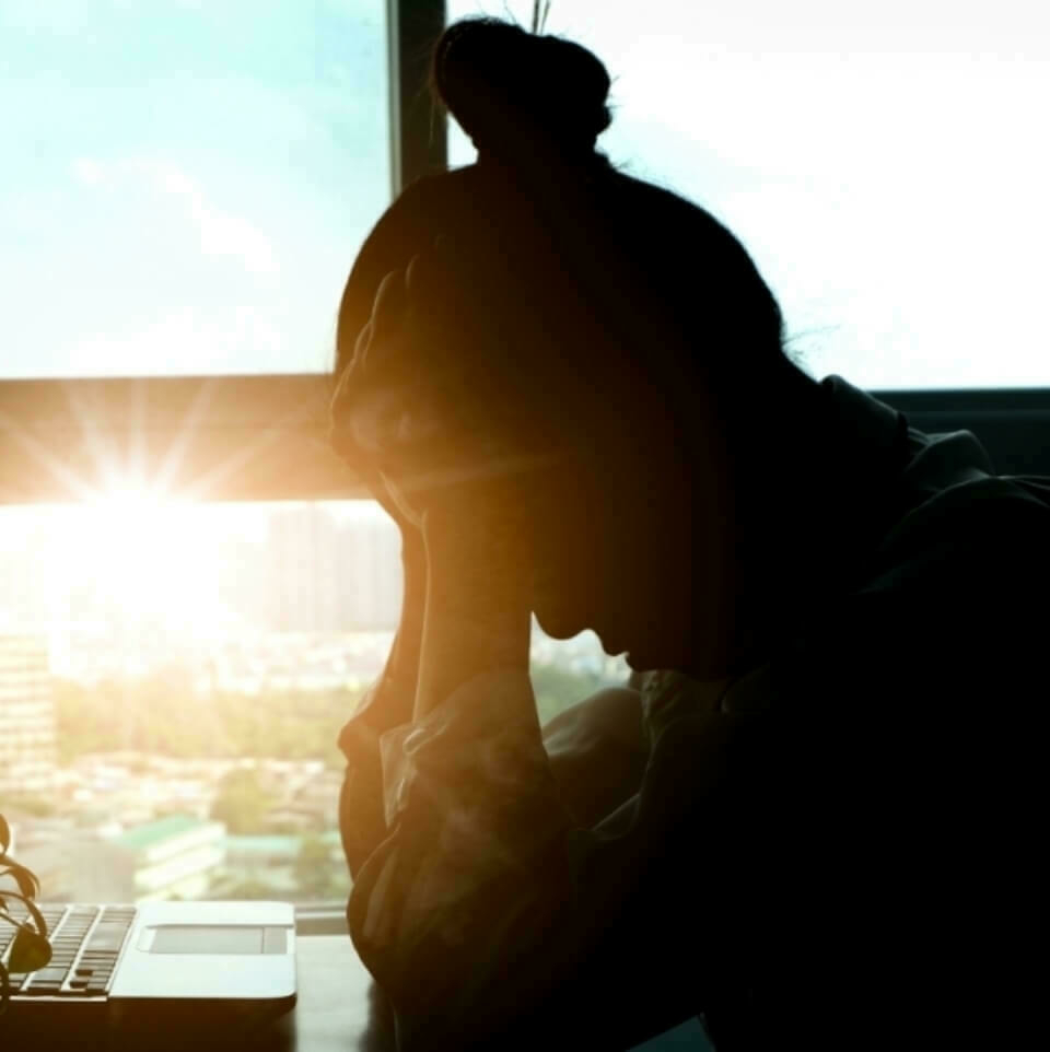 Silhouette of woman leaning over a computer.