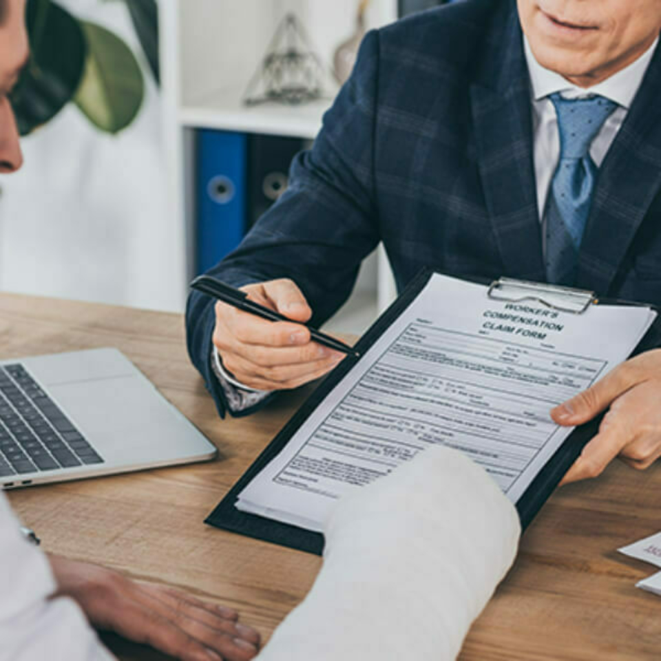 Person in suit helping another person in a cast fill out paper forms.