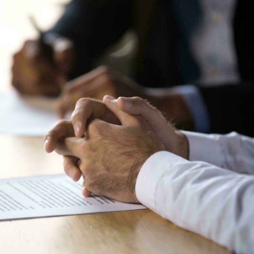 Close up of man's hands clasped on table over paperwork.