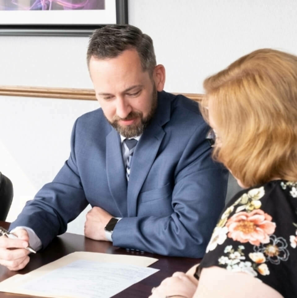 Man in a suit helping a woman fill out paperwork.