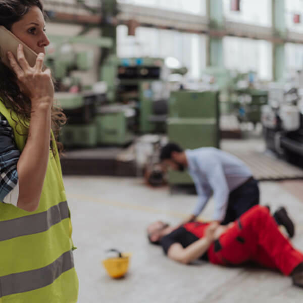 Woman on the phone in front of an injured worker on the ground.