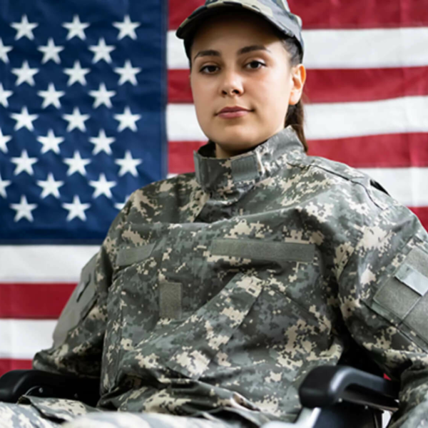 Female veteran in uniform in a wheelchair in front of the American flag.
