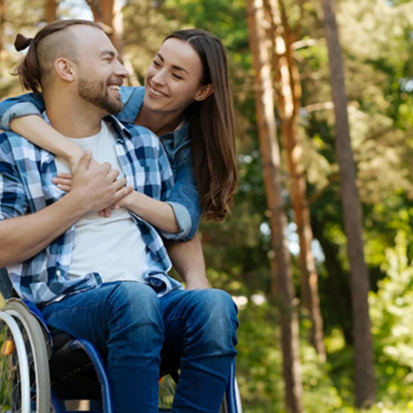 Woman hugging a man in a wheelchair from behind.