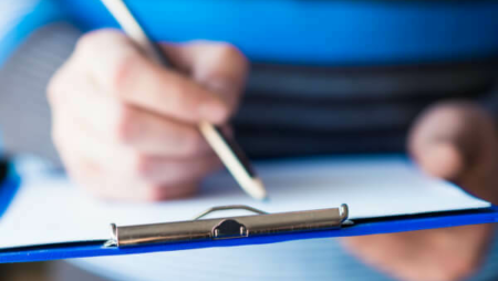 Person filling out forms on a blue clipboard.