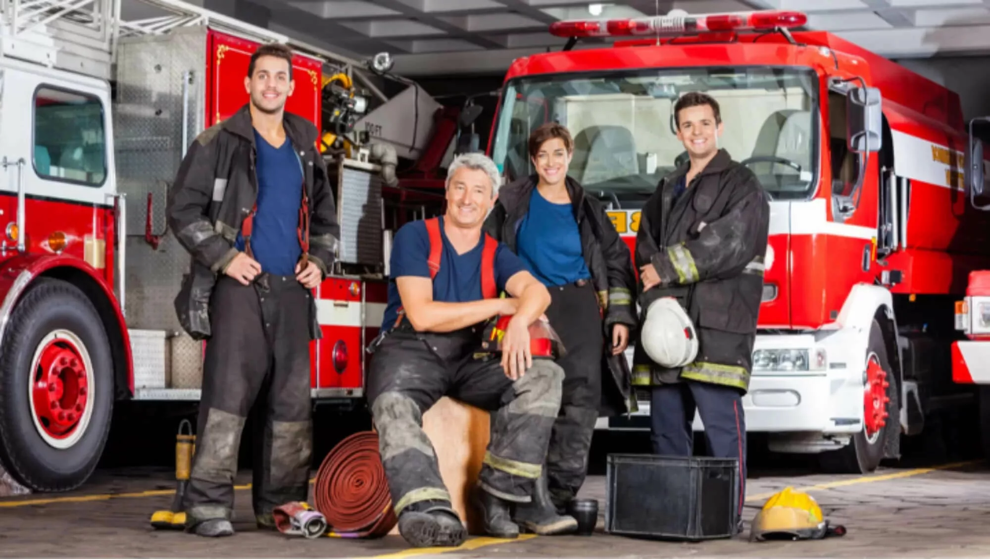 Four firefighters in uniform posing in front of a firetruck.