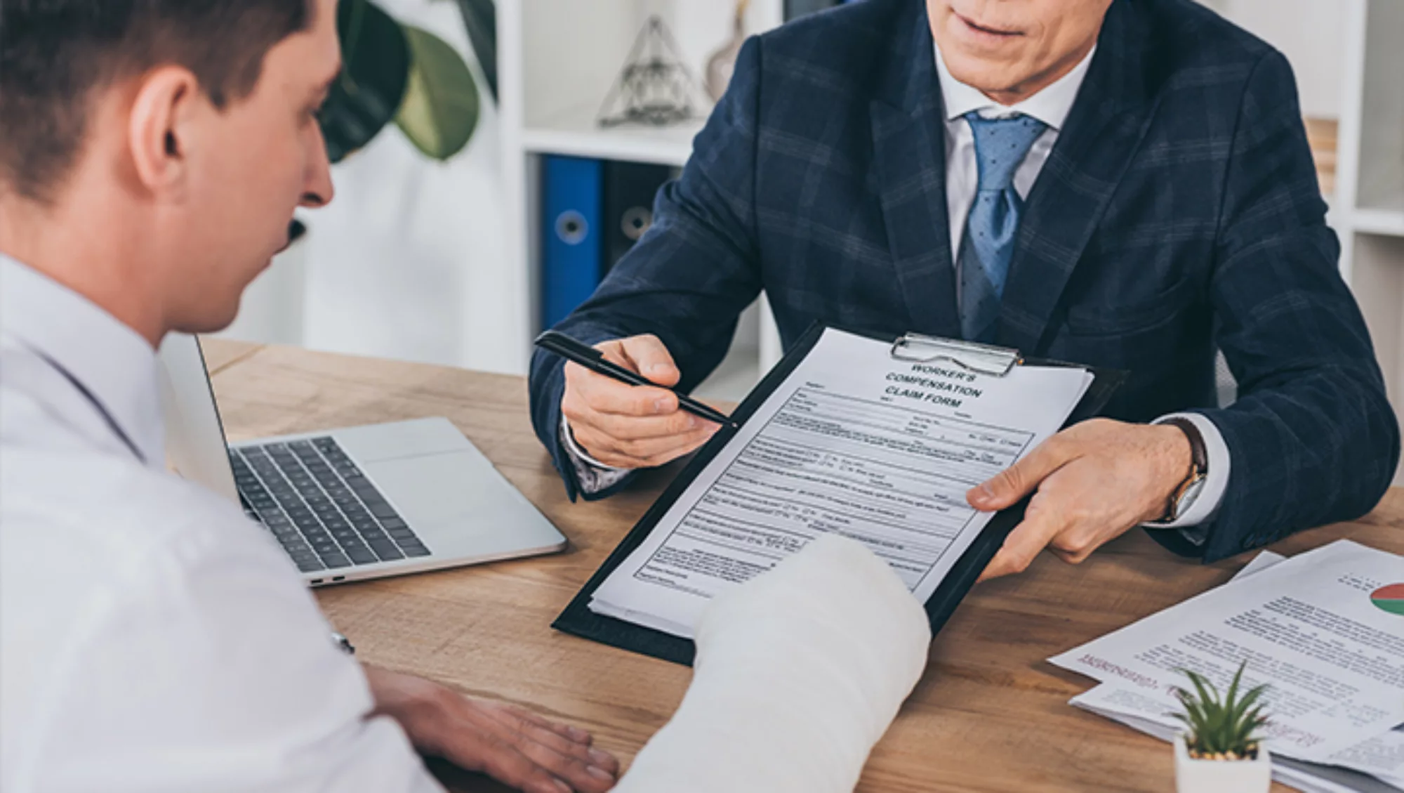 Person in a suit helping another person in a cast fill out paper forms.