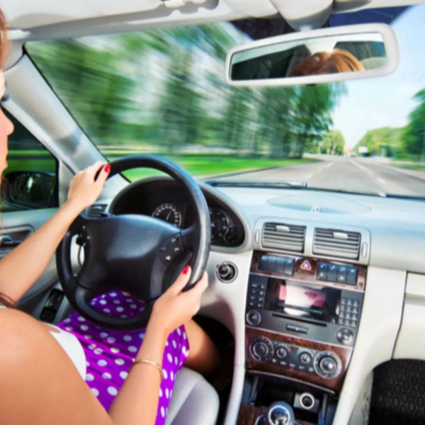 Woman in purple polka dots behind the wheel of a car, driving quickly.